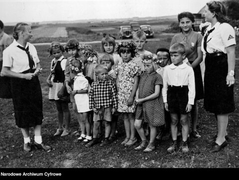 Girls from the Association of German Girls with a group of children. Some of the children are wearing flower garlands on their heads.