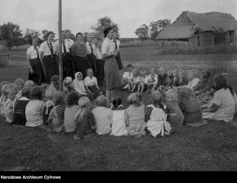 An instructor from the Association of German Girls teaches German songs to rural Volksdeutsche children in the Radom area. – National Digital Archive (Public domain) An instructor from the Association of German Girls teaches German songs to rural Volksdeutsche children in the Radom area.
